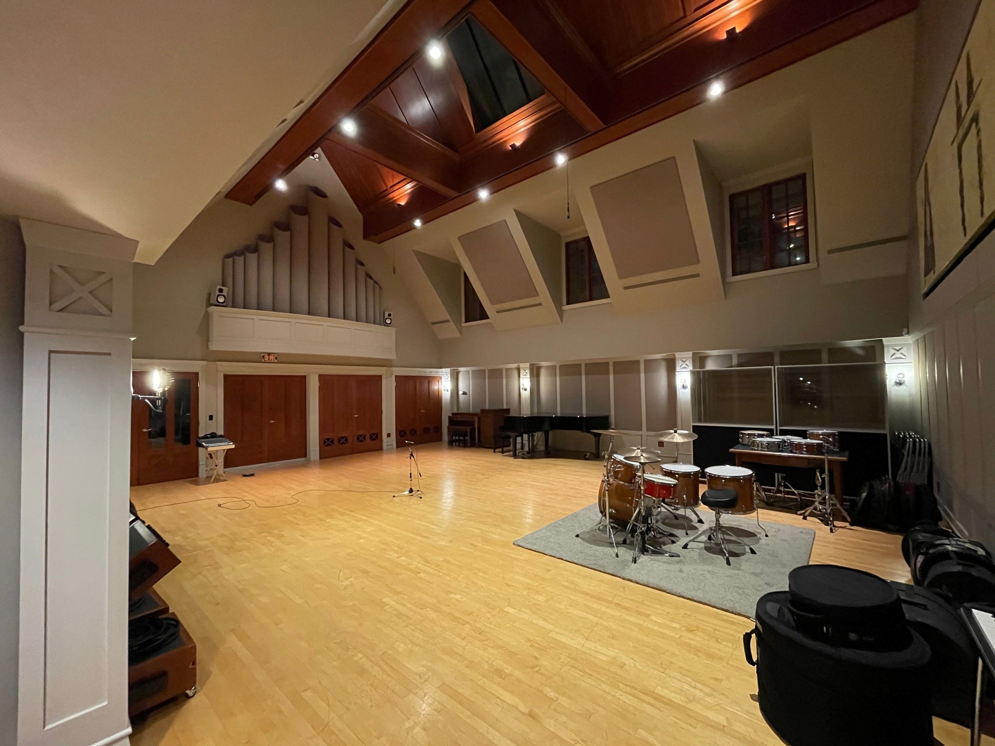 Large live recording room with high vaulted ceiling, hardwood floors, drum kit, and grand piano